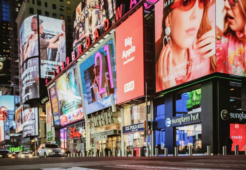 Cluster of high-resolution LED digital billboards on a busy Times Square street featuring fashion and retail brand ads.