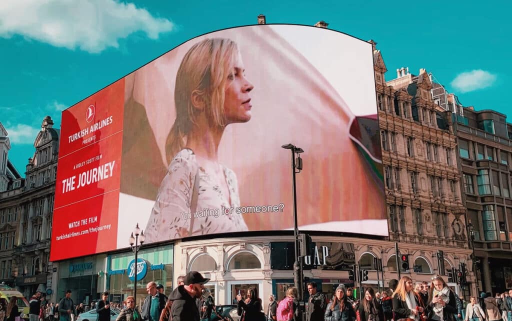 Massive curved LED digital billboard in London displaying cinematic content above a busy urban street.