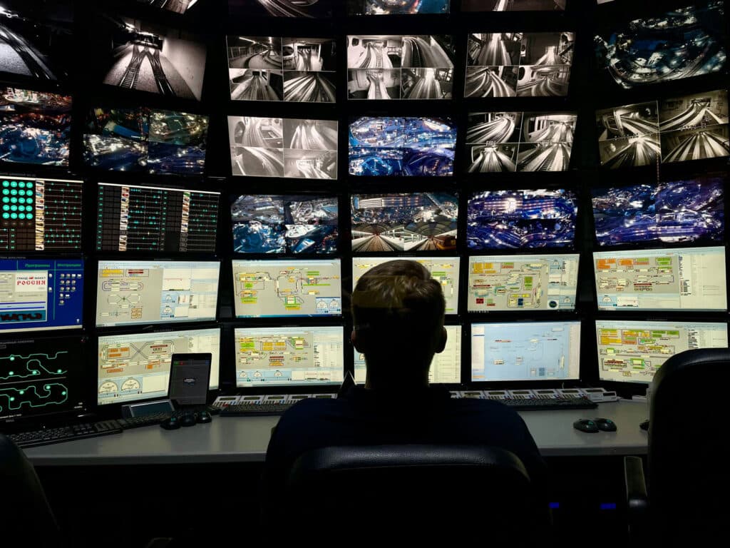 Person monitoring multiple security and traffic control screens in a command center.